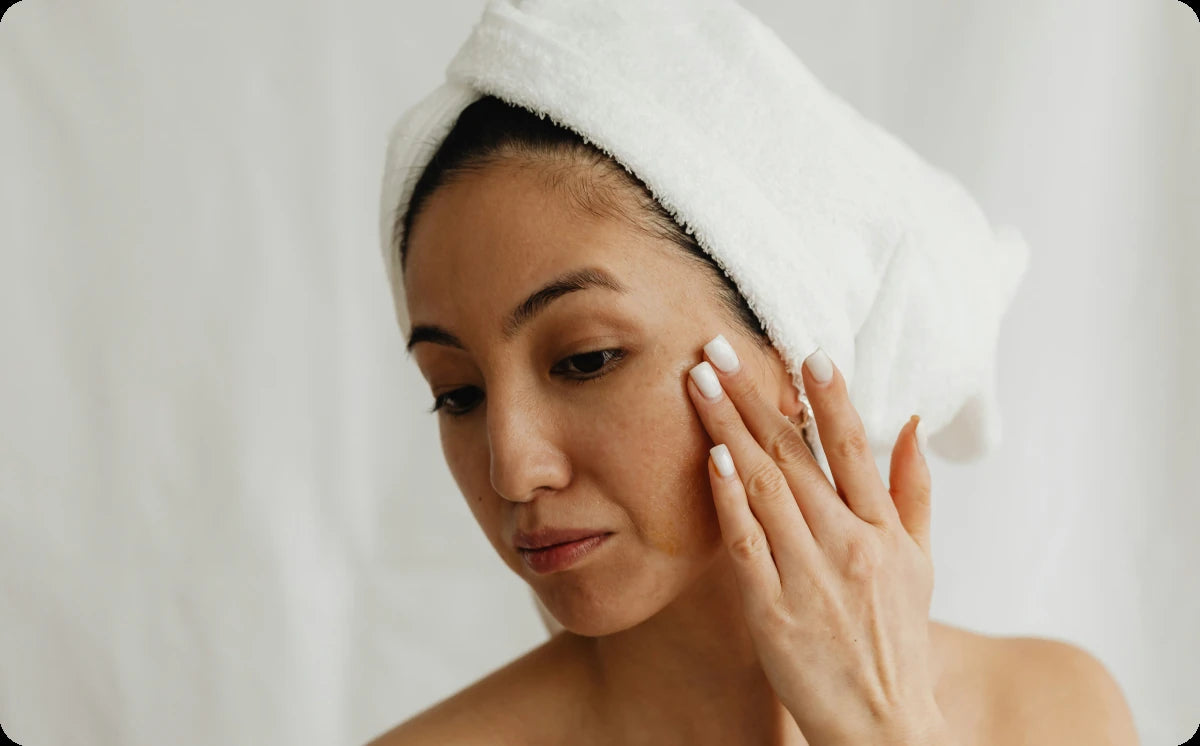 Woman with a towel wrapped around her hair applying emu oil to her cheek