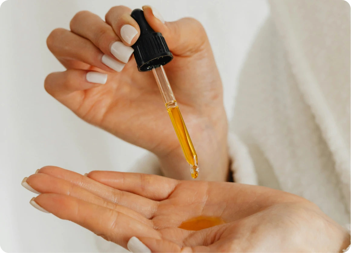 A glass dropper releasing golden emu oil into an open palm