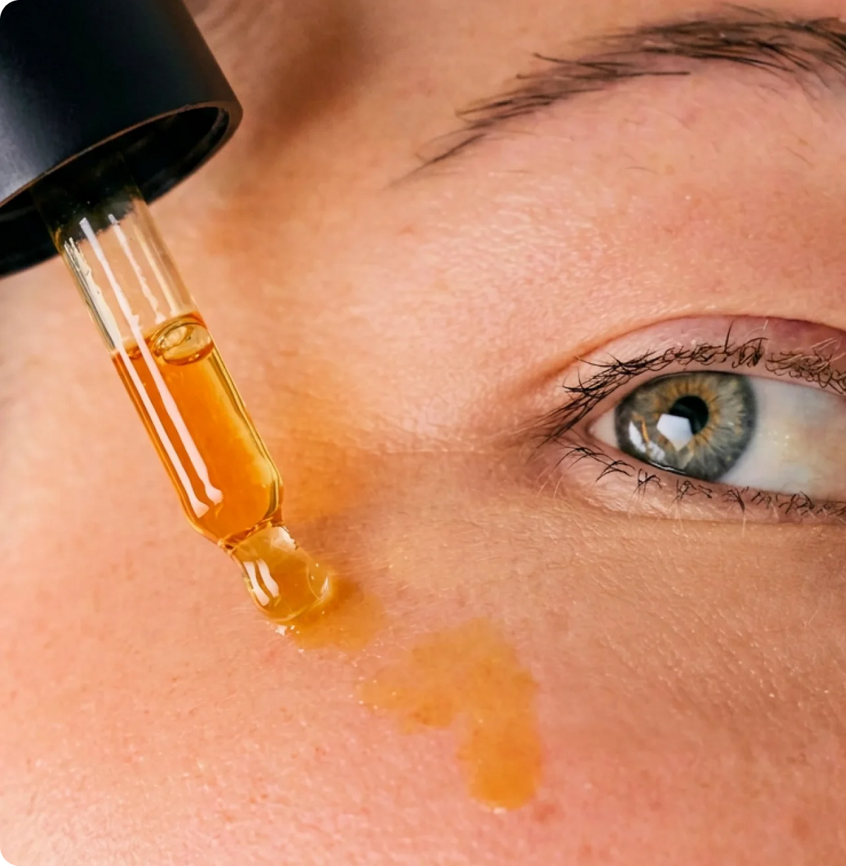 A dropper of golden emu oil held beside a person's eye