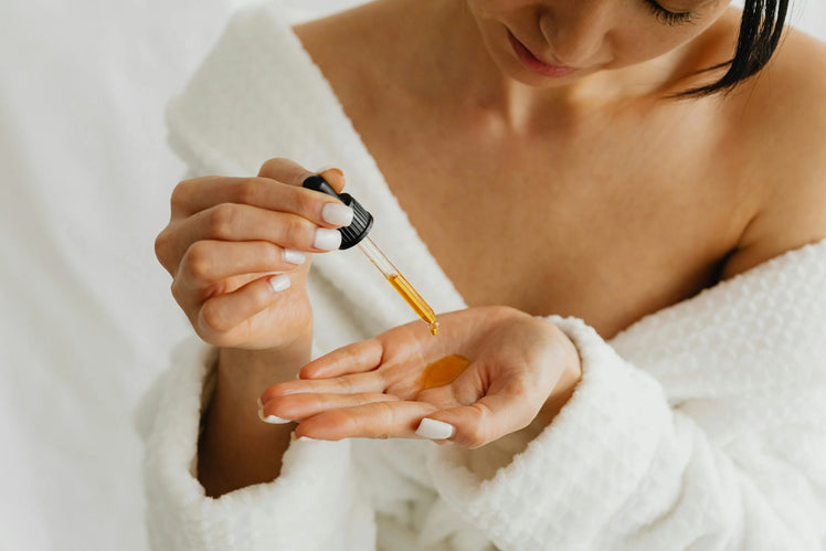 Woman in a bathrobe dispensing facial oil into her palm