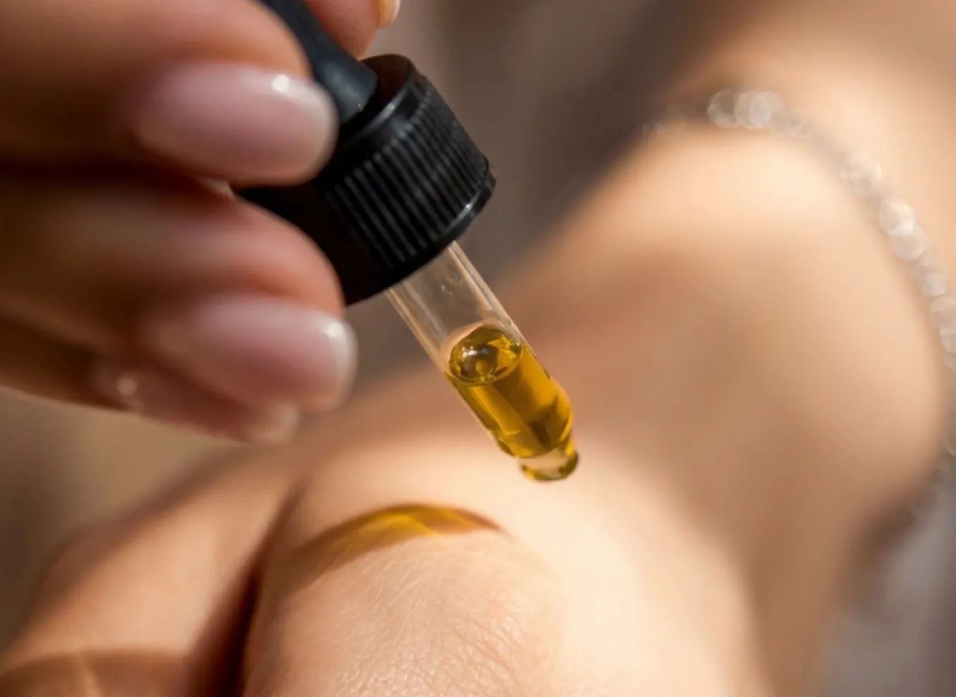 Dropper applying golden emu oil to the back of a hand