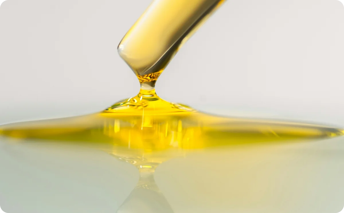 Golden emu oil dripping from a glass dropper into a shallow pool