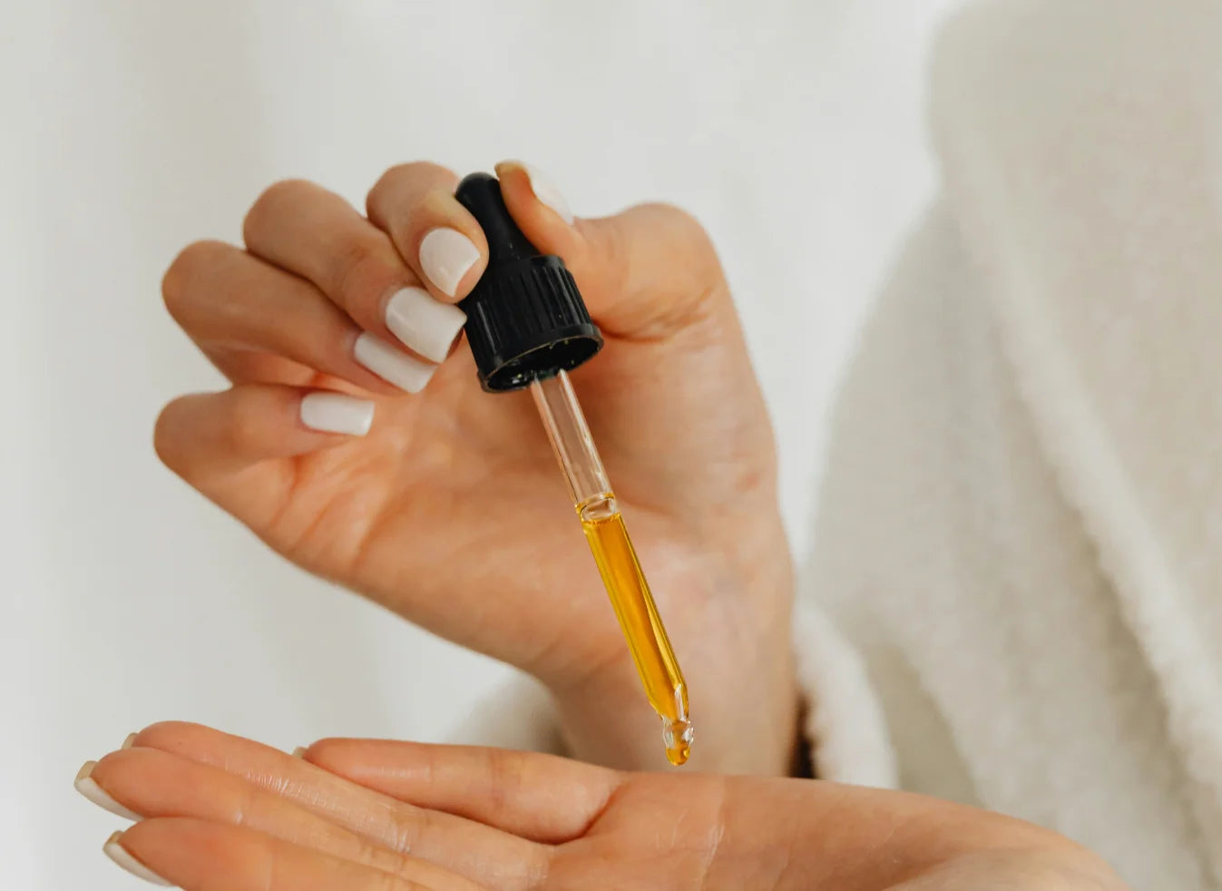 Hands holding a glass dropper filled with golden emu oil over an open palm