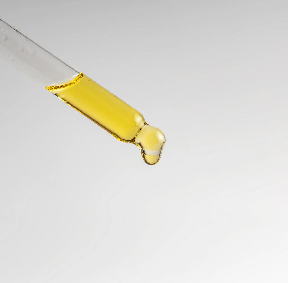 Glass dropper releasing a drop of golden emu oil