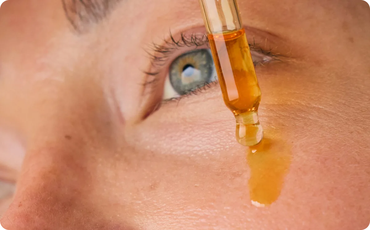 Dropper applying amber emu oil to the skin beside a woman's eye