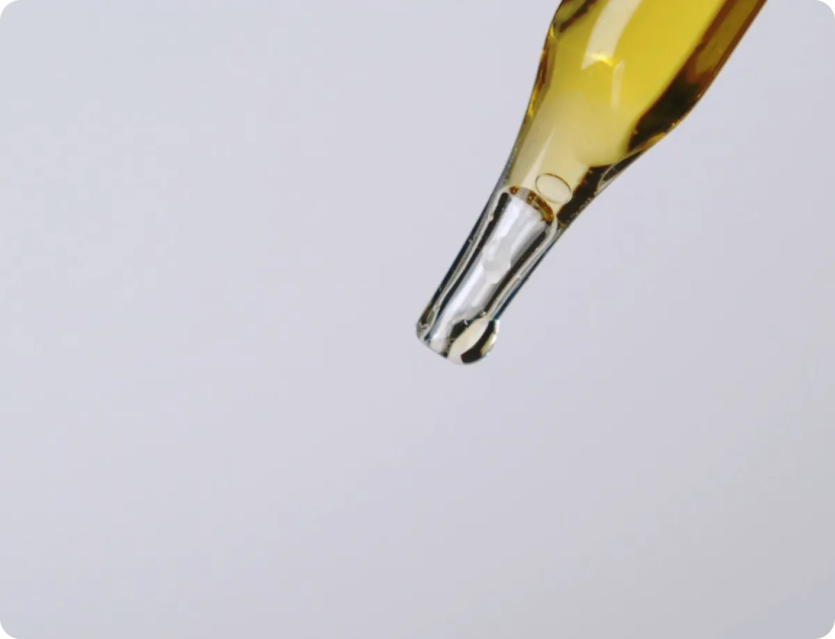 Glass dropper tip holding a drop of golden refined emu oil