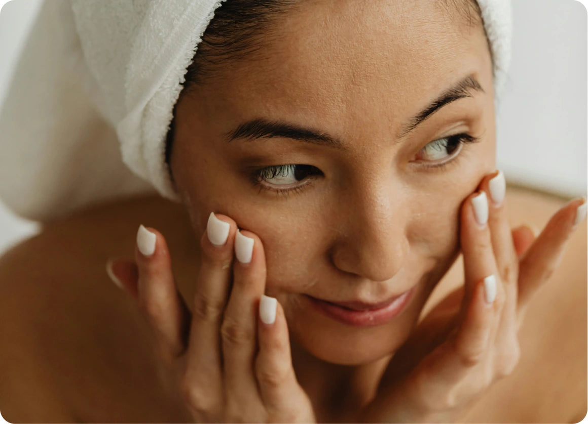 A woman with a hair towel pressing cream into both cheeks