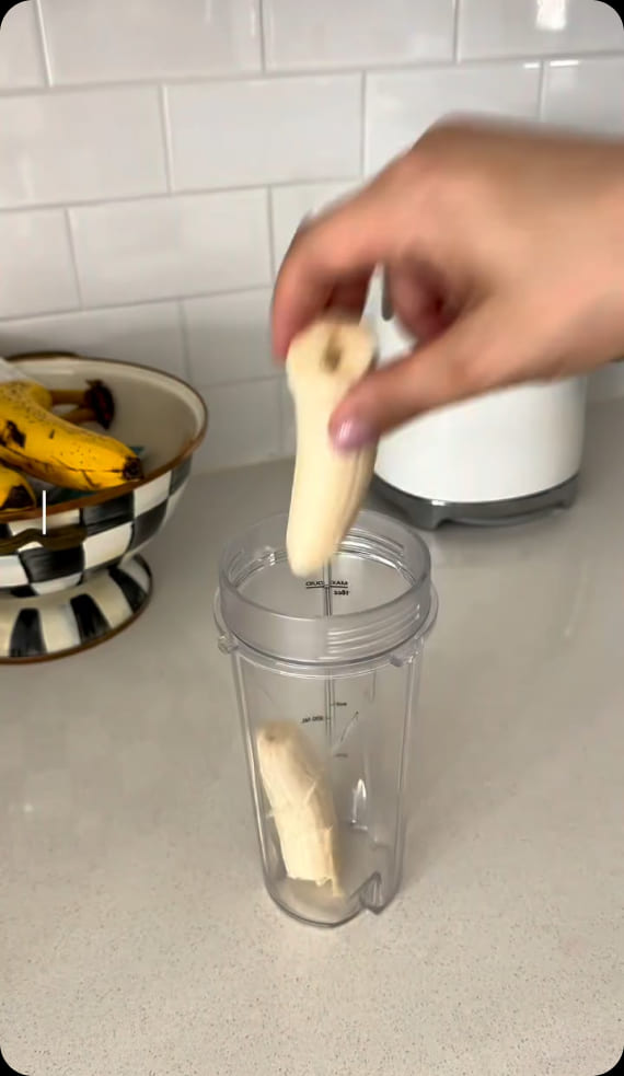 Customer video: a hand dropping a peeled banana into a blender cup on a kitchen counter
