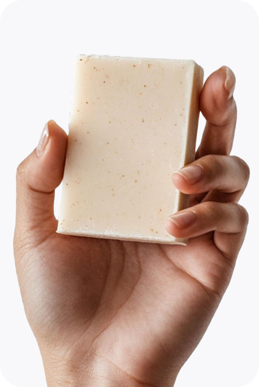 Hand holding an Emu Joy oatmeal soap bar on a soft grey card
